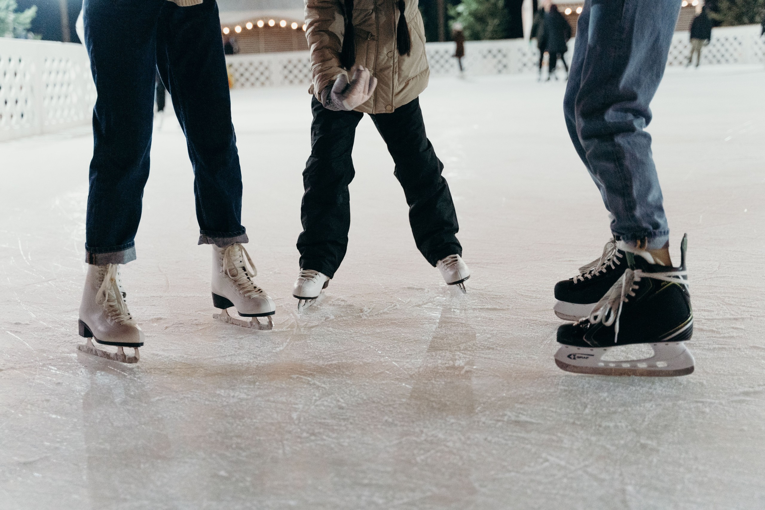 Three people ice skating on a rink, focusing on their skates.