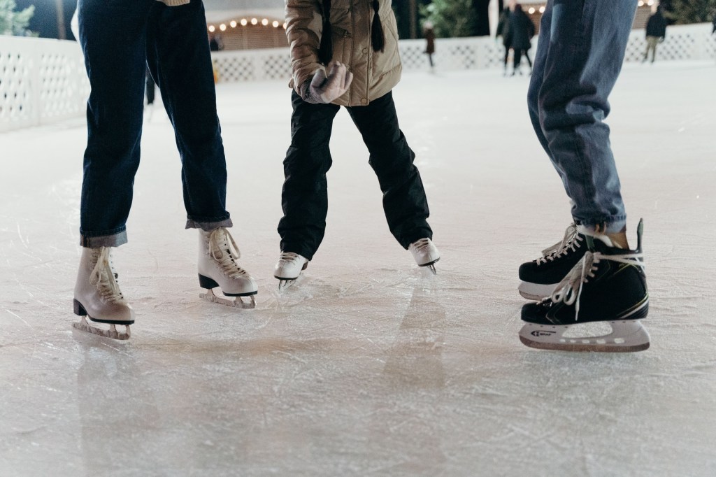 Three people ice skating on a rink, focusing on their skates.